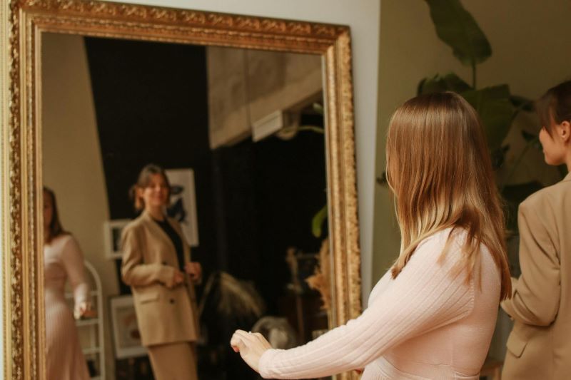 Frustrated woman checking clothing fit in front of a mirror, reflecting common UK fashion sizing issues
