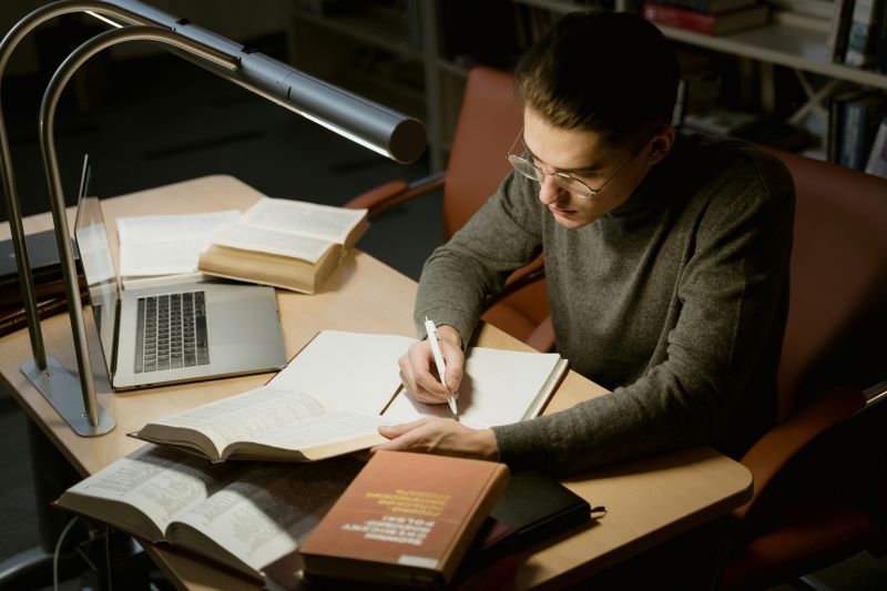 Young UK model studying at a desk with fashion portfolio and laptop, symbolising balance between modeling career and education.